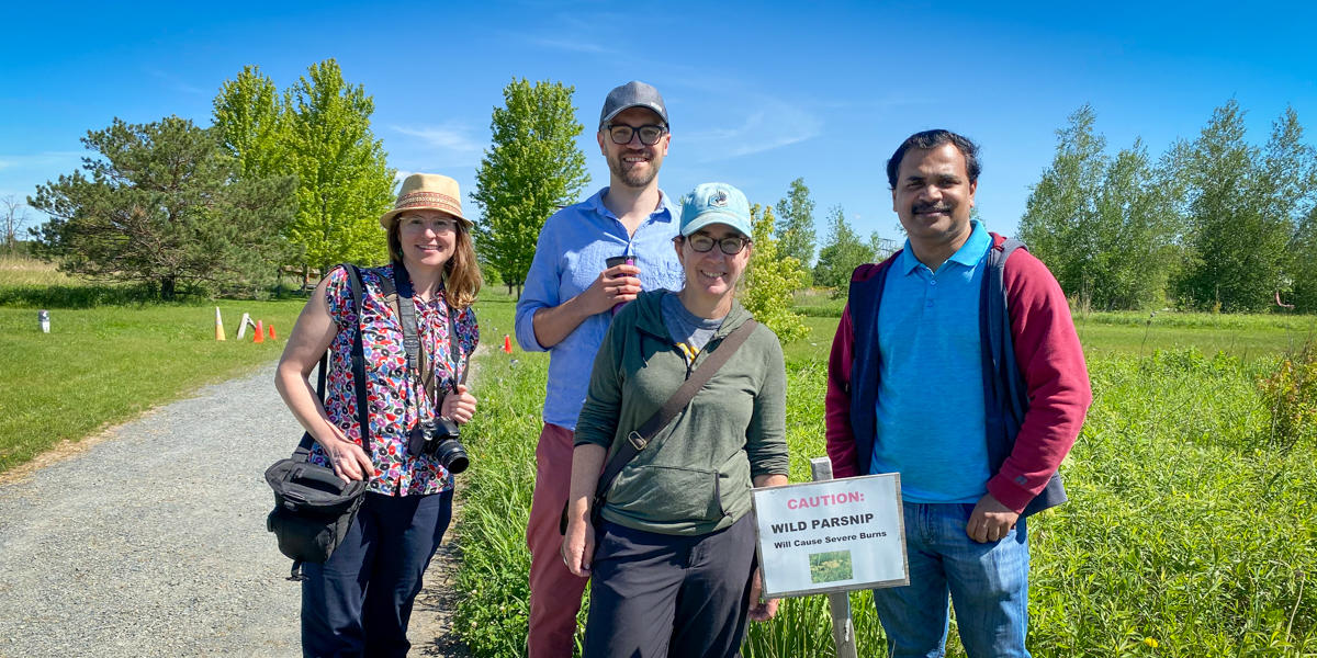 researchers pose for a photo in a field with a wild parsnip warning sign