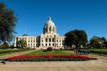 Minnesota State Capital building in St. Paul, MN. The sky is clear and blue and there are red flowers on the lawn in front of the building.