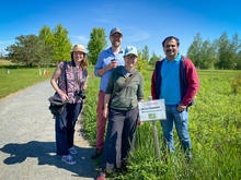 four researchers pose in a field next to a sign warning of wild parsnip